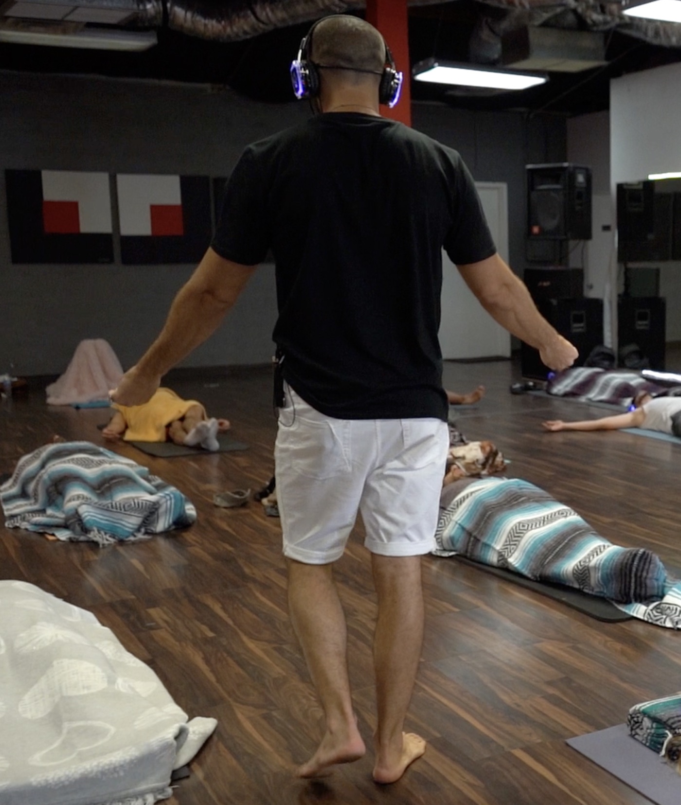 Ryan McBurney facilitating a group Breathwork session while wearing 9D-style over-ear headphones with participants resting on mats around him